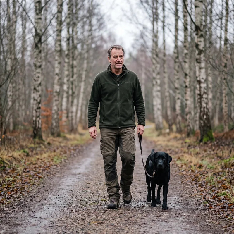 Man i 45-årsåldern promenerar med sin hund i en björkskog